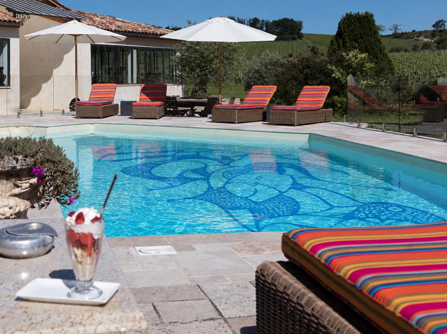 Cocktail beside the outdoor pool with its blue floor design and Château du Palanquey in the background